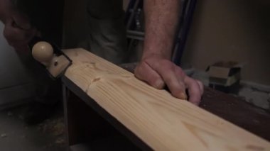 Bir adam el uçağıyla tahtayı yontuyor..