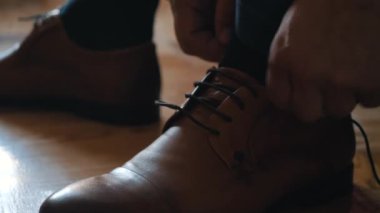 Bir adam ayakkabı bağcıklarını deri ayakkabılarla bağlar.