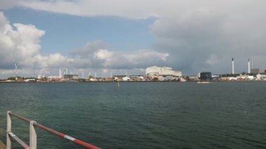 A stunning harbor view features a colorful boat near industrial structures beneath a textured cloudy sky