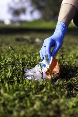 Genç bir kadının eli ormanda terk edilmiş cam ve şişeleri topluyor. Geri dönüşüm kavramı, doğa, gönüllülük.