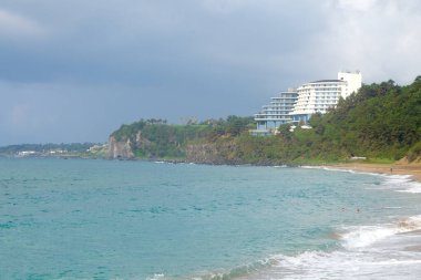 Teraslı bir tesis Jungmun Saekdal Sahili 'nin yukarısındaki kayalıklarda yer alır. Aquamarine suları, koyu kaya çıkıntıları ve alttaki kumun üzerine yuvarlanan alçak dalgalarla..