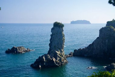 Yükselen deniz yığını Oedolgae Kayası, zirvesinde bitki örtüsü ve Seogwipo 'daki körfezi çevreleyen kayalıklarla mavi denizden dik bir şekilde yükselir..