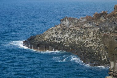 Dalgalar Daepo Jusangjeolli 'deki dikey bazalt sütunlara çarparak engebeli kayaları oluşturur..