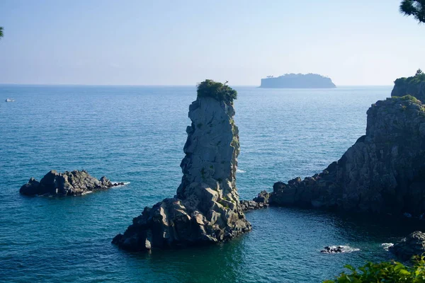Yükselen deniz yığını Oedolgae Kayası, zirvesinde bitki örtüsü ve Seogwipo 'daki körfezi çevreleyen kayalıklarla mavi denizden dik bir şekilde yükselir..