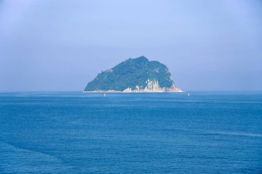 Seopseom Adası Seogwipo 'nun sakin mavi suyundan yükseliyor, ormanlık yamaçları ve solgun uçurumları denize karşı duruyor..