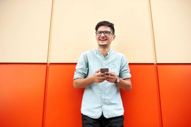 Cep telefonunu sokakta turuncu duvarı kullanarak yakışıklı genç adam portresi