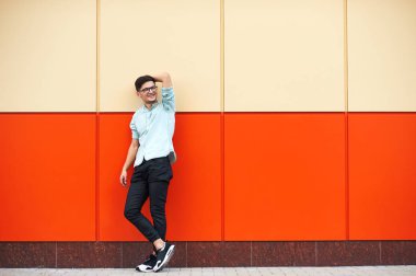 Genç yakışıklı oğlan mavi tişörtlü, güneş gözlüğü, yanındaki turuncu duvar arka plan ayakta