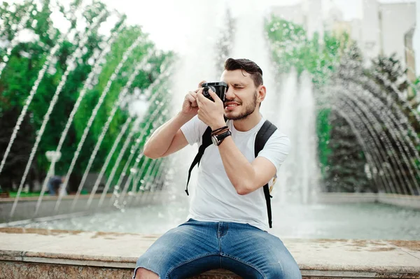 Schöner junger Mann beim Fotografieren im Park. stylischer Junge im weißen T-Shirt, mit Rucksack, der Fotos macht. — Stockfoto