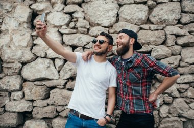 Portre bir iki genç erkek bir selfie birlikte taş duvar arka plan üzerinde duran süre alarak heyecanlı.