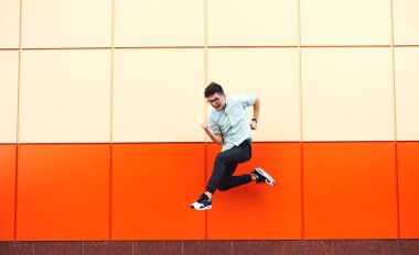 Renkli duvara atlama gözlüklü genç ve güzel adam. Hipster ornage arka plan üzerinde hareket