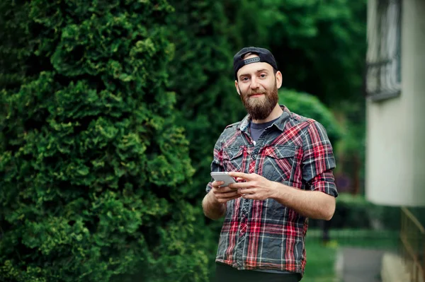 Élégant hipster avec une barbe dans une tenue décontractée en utilisant le téléphone et en regardant la caméra — Photo