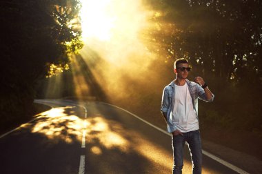 Yakışıklı delikanlı mavi tişört, Beyaz tişört ve güneşli arka plan üzerinde poz güneş gözlüğü.