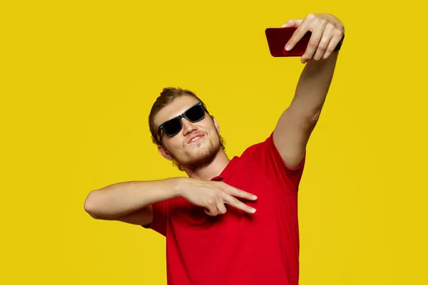 Imagem de jovem caucasiano feliz posando isolado sobre fundo amarelo tirar uma selfie por telefone mostrando gesto de paz . — Fotografia de Stock