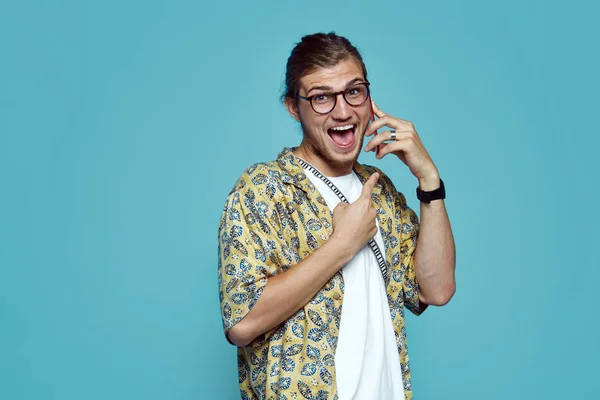 Portret podekscytowany młodych Brodaty mężczyzna rozmowy na telefon komórkowy, wskazując palcem na telefon na białym tle niebieski — Zdjęcie stockowe