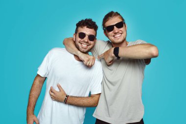 İki genç hipster adam iyi ilişki ve samimi dostluk, embarce sahibiz ve gladfully üzerinde mavi arka plan gülümsemek