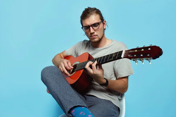 Csinos, fiatal kaukázusi Férfi gitározni ülve, elszigetelt, felett kék háttér. — Stock Fotó
