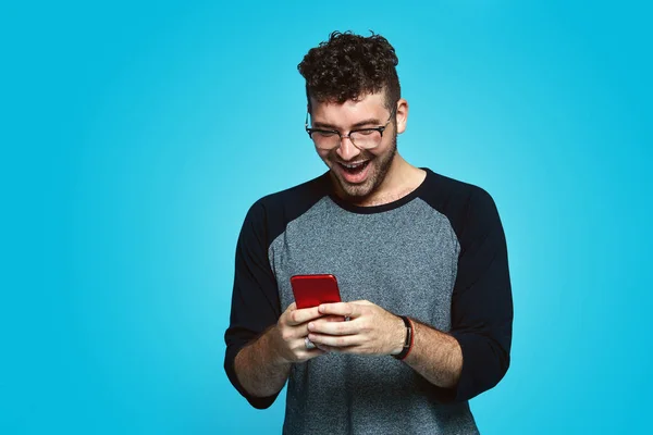 Mavi kopya alanı duvarla karşı duran, seyir smartphone.d, perde genç yakışıklı hipster adam kutluyor