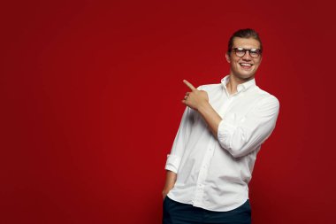 Casual yakışıklı gülen ve işaret eden beyaz gömlek giymiş gözlük ile olan ayakta kırmızı zemin üzerine yaptı.
