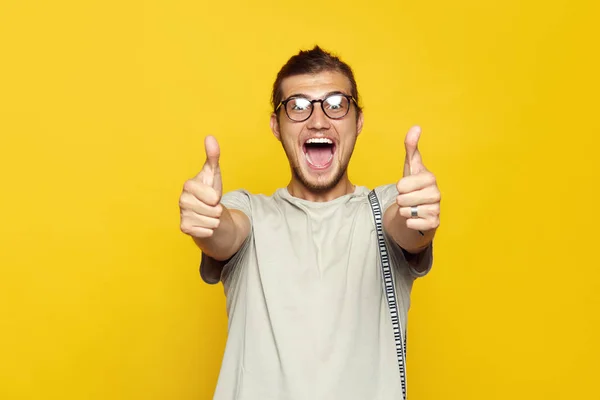 Atractivo hombre caucásico sonriendo y mostrando el pulgar hacia arriba gesto con ambas manos sobre el fondo amarillo y mirando a la cámara . — Foto de Stock