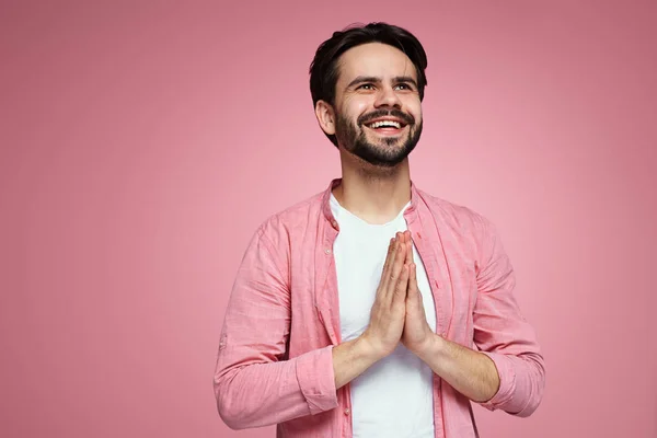 Barışçıl genç hippi ellerini birarada tutar ve gülümserken pembe arka planda izole bir şekilde yukarı bakar..