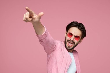 Kamera parmak işaret, çığlık ve pembe arka plan üzerinde duran pembe tişörtlü yakışıklı adam.