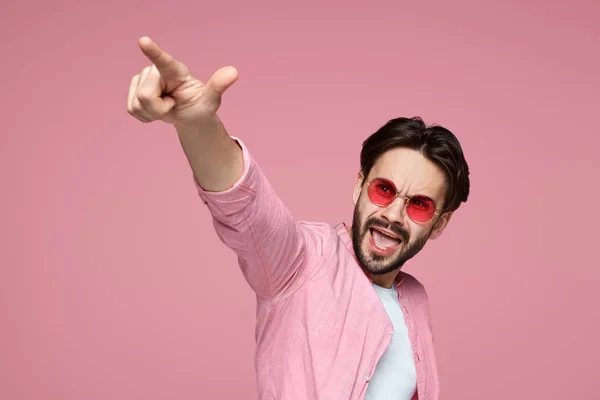 Bonito homem de camisa rosa apontando o dedo para a câmera, gritando e de pé sobre o fundo rosa . — Fotografia de Stock