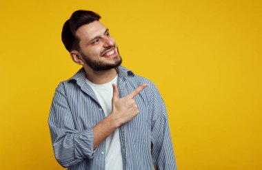 Neşeli yakışıklı adam çizgileri ile klasik gömlek giyen ve turuncu arka plan üzerinde mutlu bir şekilde işaret.