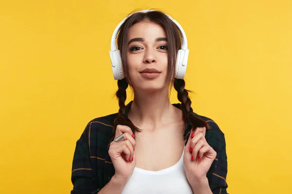 Beyaz kulaklıkile Çekici hipster kız, müzik dinler ve mutlu hissediyor, sarı duvar üzerinde izole onu midilli kuyrukları ile oynarken