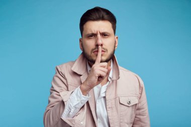 Çekici adam Hush jest gösterir, fotoğraf makinesinde hayrete ifade ile görünüyor, dedikodu korktugu, mavi arka planda izole.