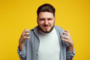 Genç kızgın erkek jestleri sinirli, ifade olumsuz duygular, Casual mavi gömlek giymiş, sarı stüdyo duvara karşı pozlar.