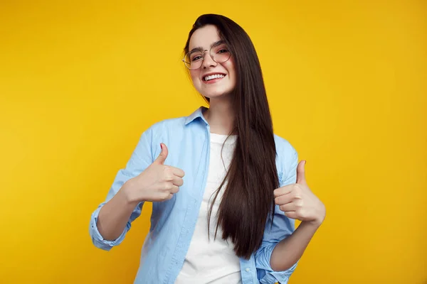Gözlüklü neşeli çekici kadın sarı arka planda izole başparmak kadar gösteren