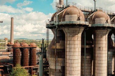 Industrial gas holders rusty towers factory landscape. Wide view of an old industrial complex with large cylindrical gas tanks, weathered steel structures and industrial architecture against a cloudy sky