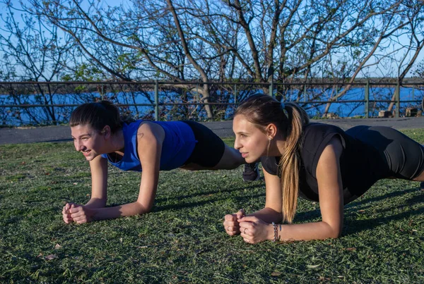 Two beautiful young women enjoying outdoor fitness in park, healthy and active living.Beautiful river background. Active lifestyle outdoor. Horizontal shot