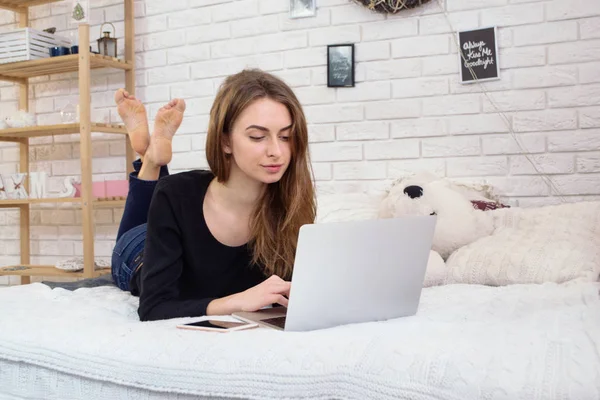 Yatağın üstünde Laptop ile iş genç kadın. Güzel kız çalışma evde Compute kullanarak