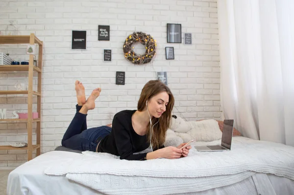 Güzel kadın Smartphone yatak odasında kulaklık ile müzik dinleme. Kız kullanarak cep telefonu ve yatağa rahatlatıcı