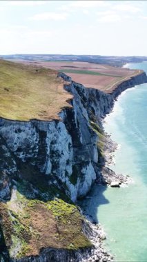 Experience the breathtaking cliff formations and vibrant greenery at Cap Blanc Nez in France. Watch as the waves crash against the stunning shoreline under a clear sky.