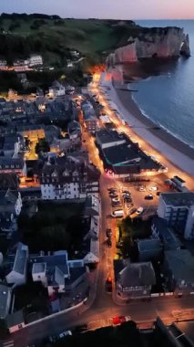 Witness the enchanting evening view over Etretat as the sun sets, illuminating the coastal cliffs and town streets. Experience the relaxation of this picturesque French location.