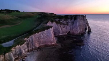 Experience the breathtaking beauty of the Etretat cliffs as the sun sets over the horizon, casting vibrant colors across the sky.