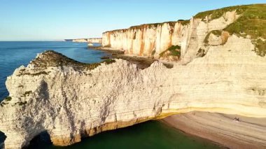 Explore the stunning cliffs of Etretat in France from above during sunset. The golden light highlights the unique rock formations and calm sea, creating a serene atmosphere.