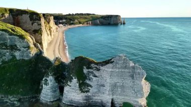Experience the breathtaking aerial view of the Etretat cliffs in France. The captivating coastline reveals sandy beaches and dramatic rock formations under a beautiful sky during sunset.
