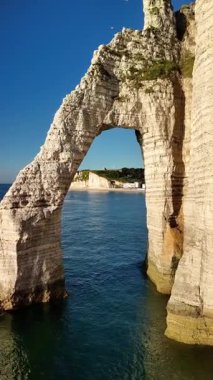 Witness breathtaking aerial views of the iconic cliffs of Etretat in France, showcasing their unique shapes and the sparkling blue sea below under clear skies.