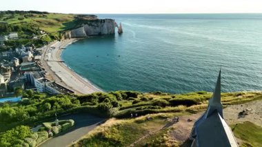 Witness the breathtaking cliffs and tranquil beach of Etretat, France from above as the sun sets over the calm waters. Experience the natural beauty and charm of this coastal gem.