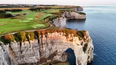 Marvel at the dramatic cliffs of Etretat in France, showcasing their unique formations and vibrant landscape. Experience the serene beauty of the coast during sunset.