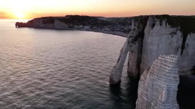 Experience the beauty of Etretat as the sun sets over the dramatic cliffs and calm waters. This aerial view showcases the natural wonders and coastal charm of this French destination.