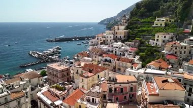 Discover the stunning beauty of Amalfi coast in Italy through an aerial view that highlights colorful homes, crystal-clear waters, and lively boat activity along the picturesque coastline.
