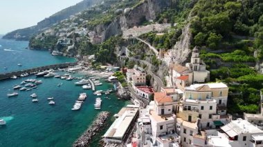 This captivating aerial view captures the beauty of the Amalfi Coast, featuring colorful cliffside villages, luxurious yachts, and the sparkling sea under bright sunlight.