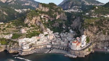 Discover the beauty of the Amalfi Coast with this aerial view highlighting the dramatic cliffs and picturesque village nestled along the coastline, surrounded by lush greenery and azure waters.