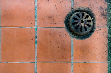 Kahverengi seramik zeminde paslı metal drenaj kapağı