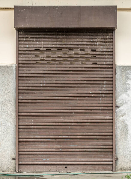 Old brown roller shutter door on white concrete wall