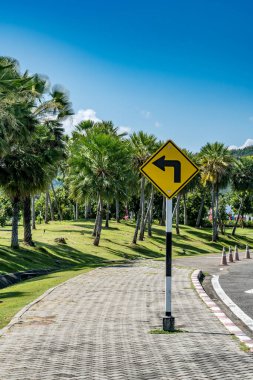 Sarı Sola dön kaldırımdaki trafik işaretinden mavi gökyüzü arkaplanındaki parkta